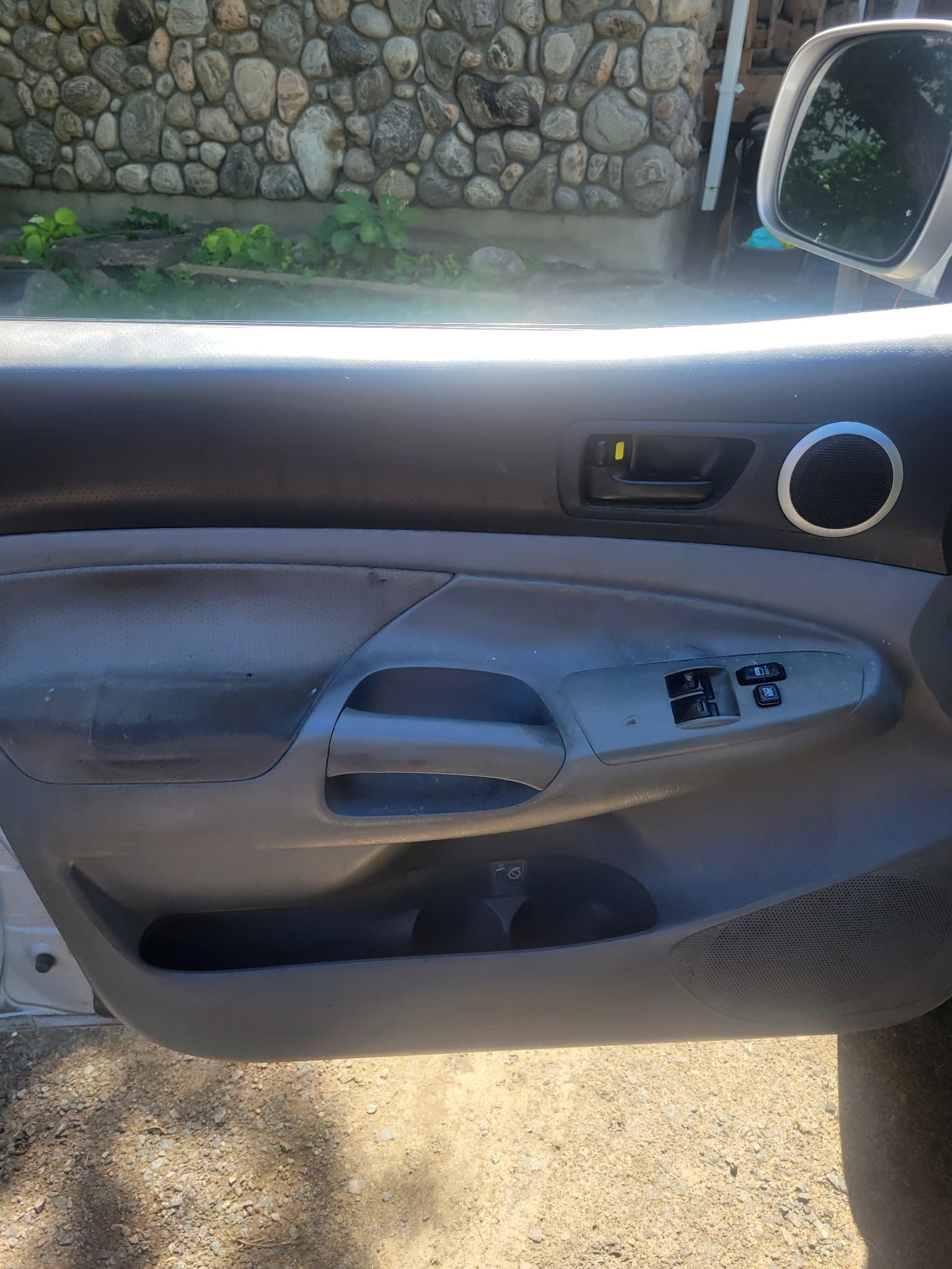 Interior of a gray car door showing window controls, door handle, and a storage bin.