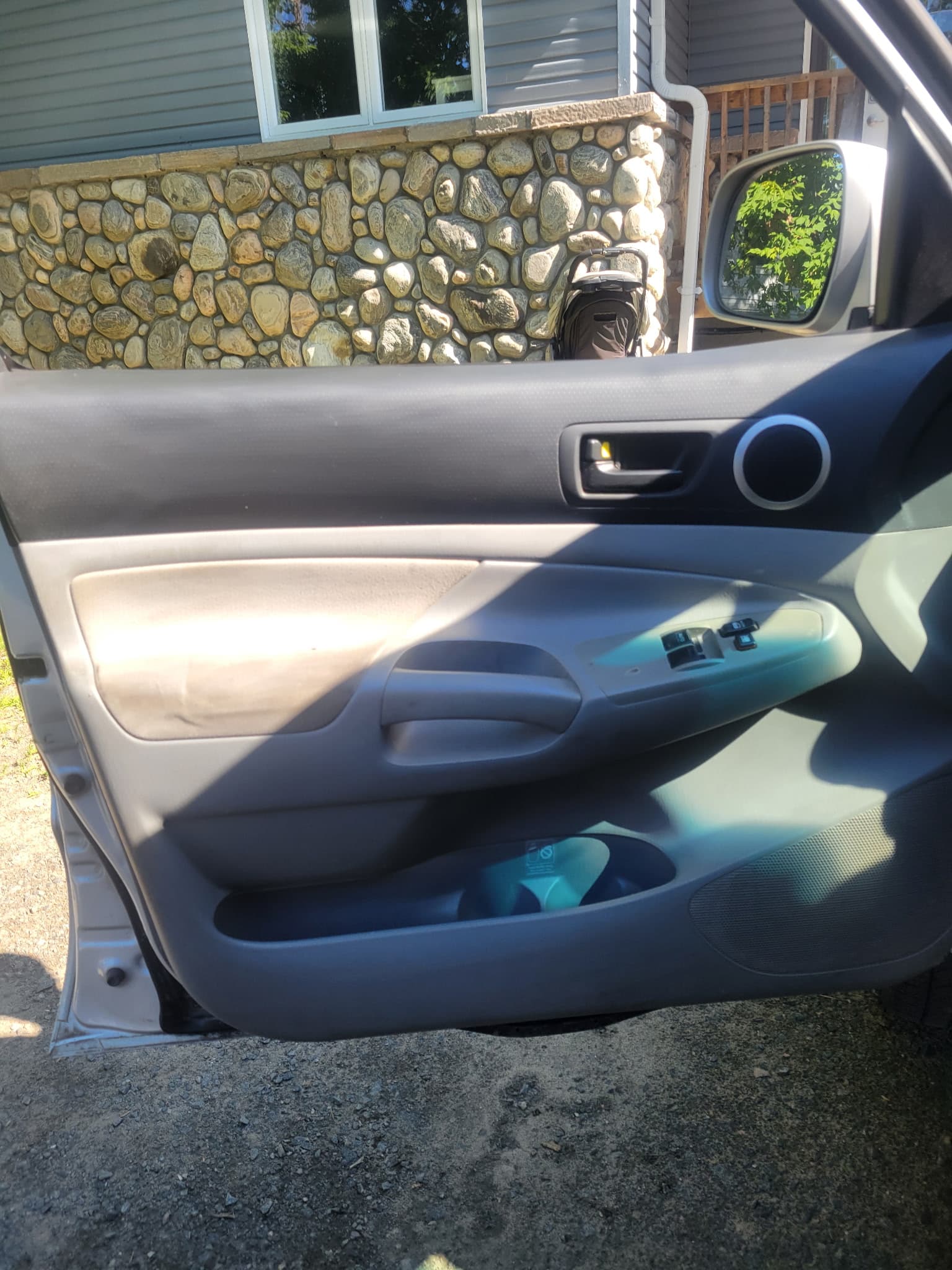 Open car door with grey and tan panels parked in front of a stone wall.