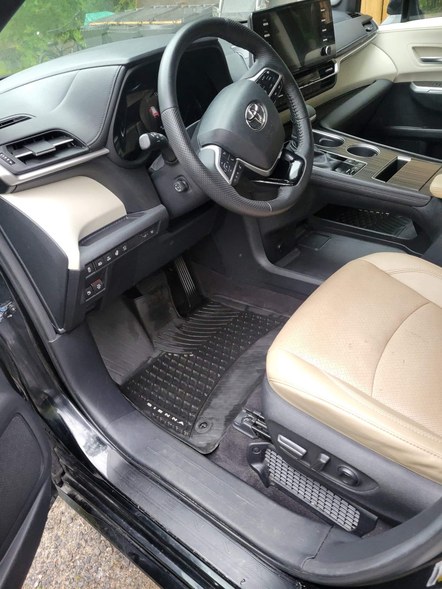Toyota Sienna driver's side interior with tan leather seats and black rubber floor mats.