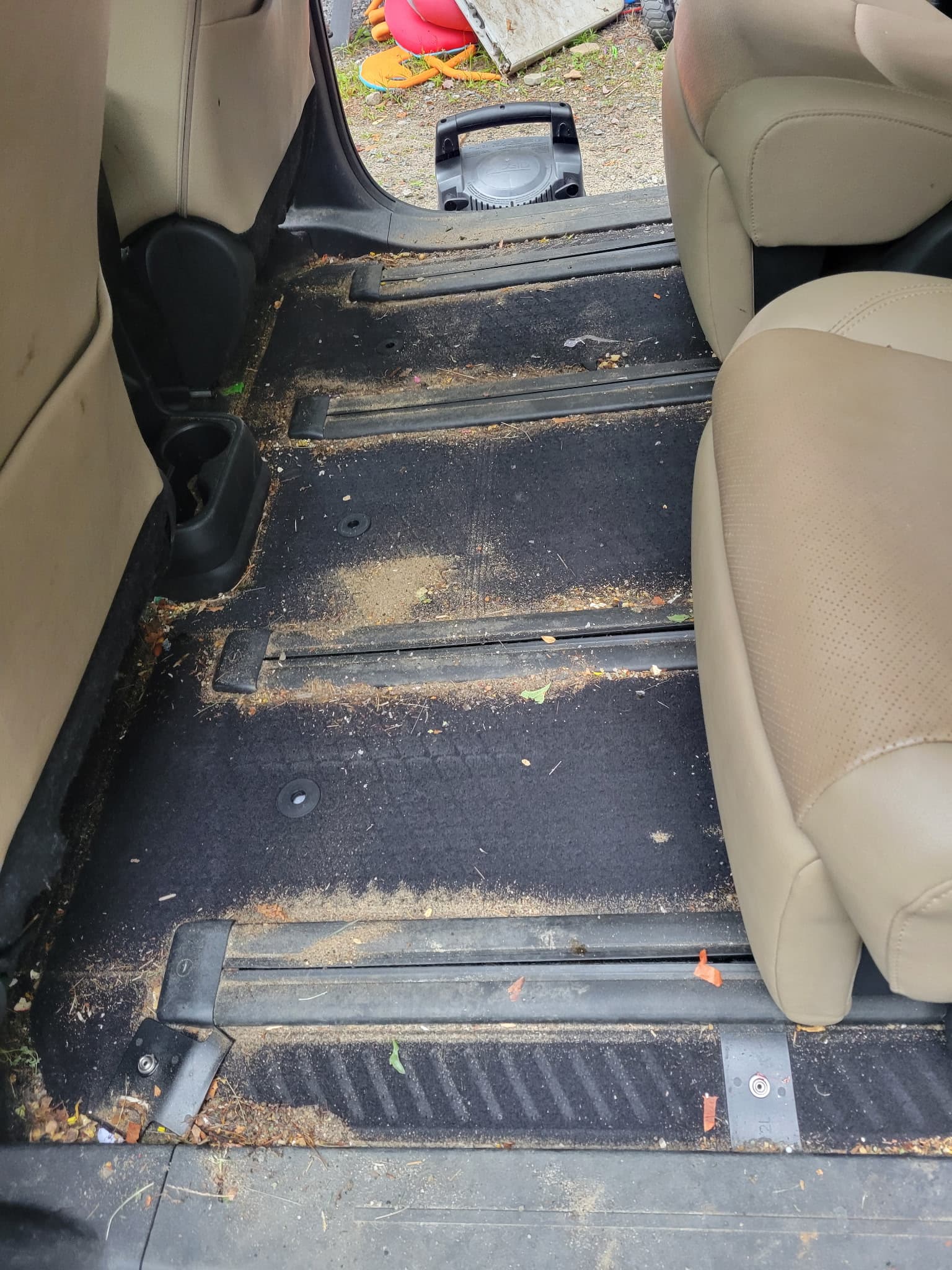 Dirty black carpeted floor of a minivan with tan seats and debris on seat tracks.