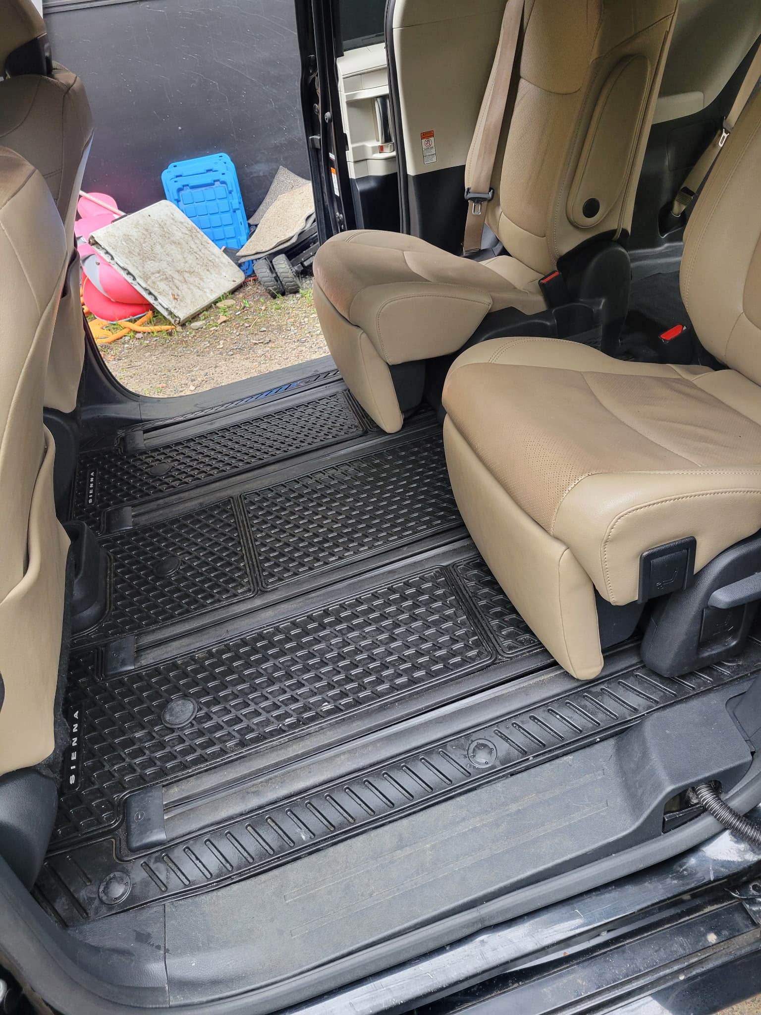 Tan leather captain's chairs and black all-weather rubber floor mats inside a Toyota Sienna minivan.