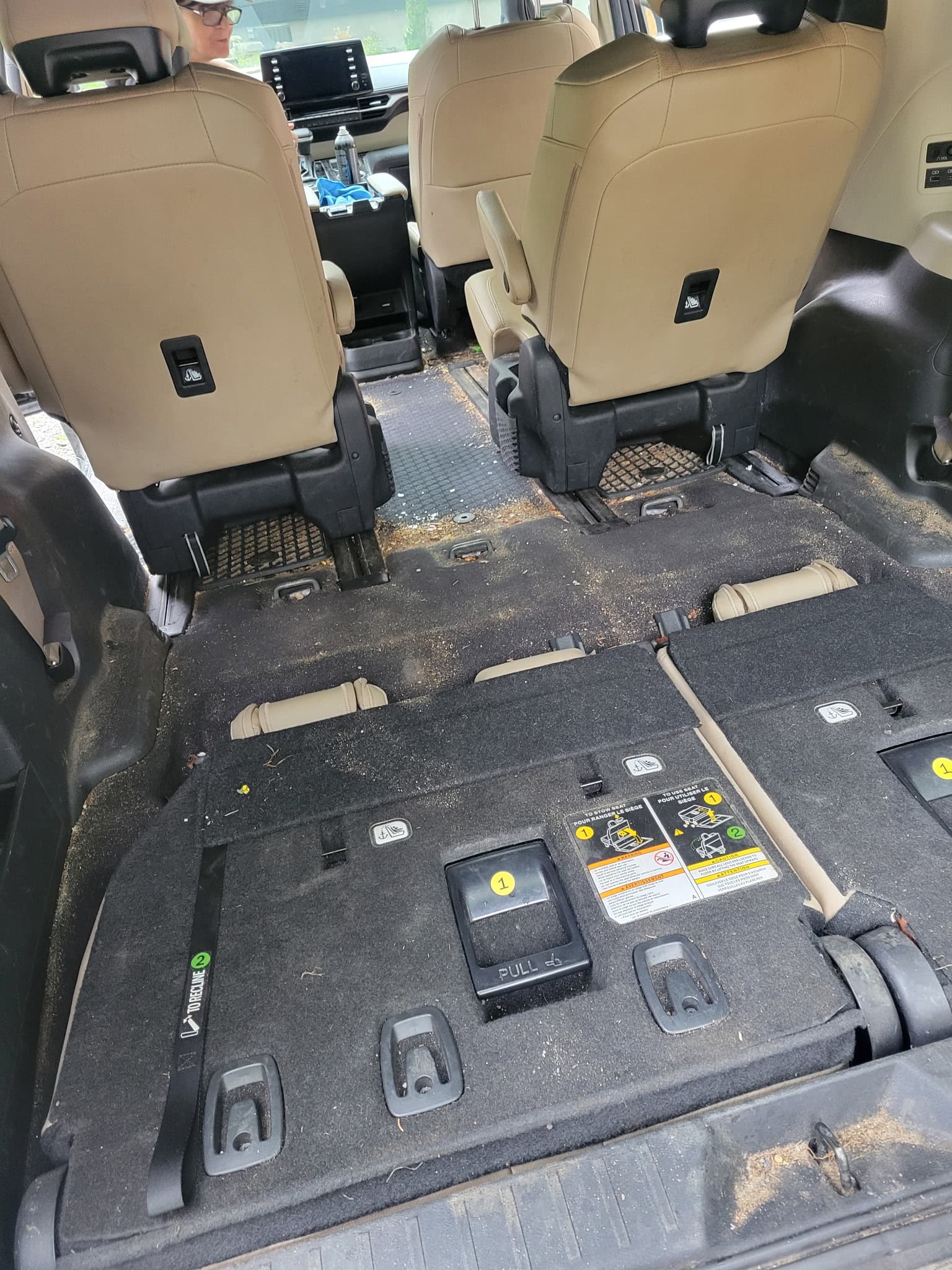 Dirty car interior with crumbs and debris scattered across the black carpet and tan seats.
