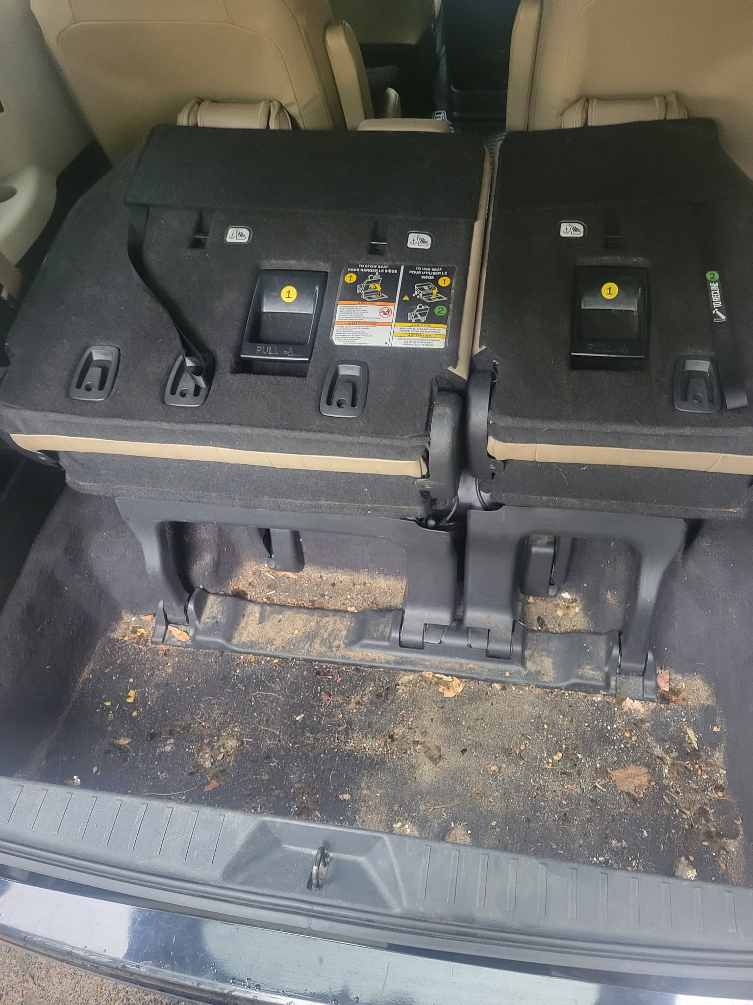 Dirty vehicle trunk with folded black seats and debris scattered across the carpeted floor.